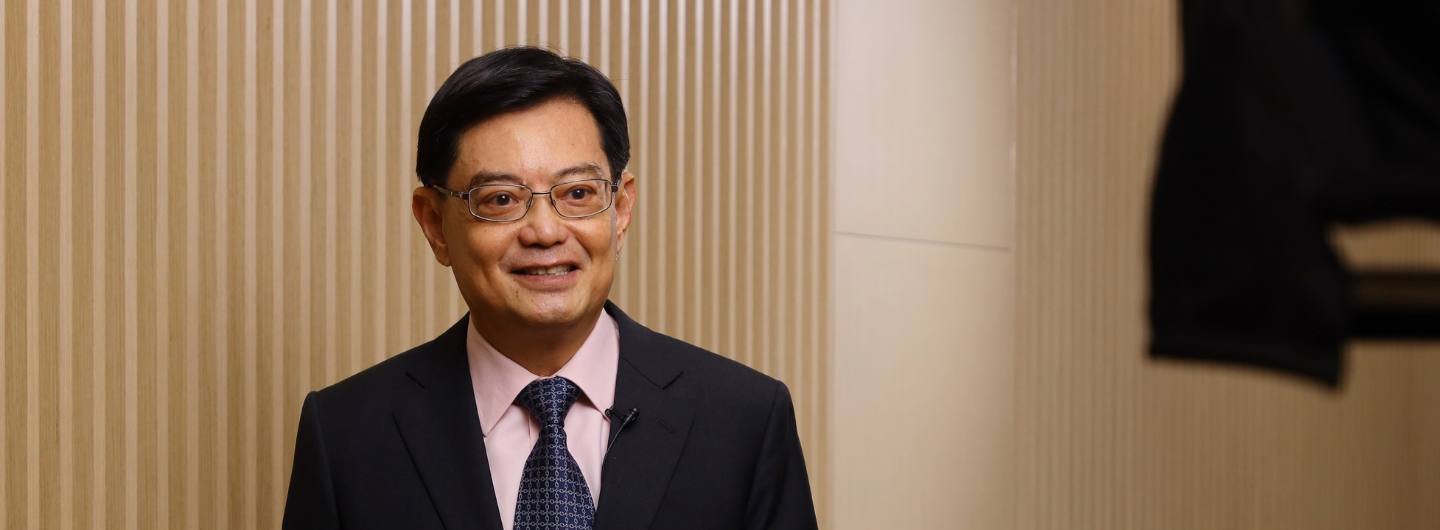 Man in suit, glasses, smiles. Background is light-colored with vertical stripes.
